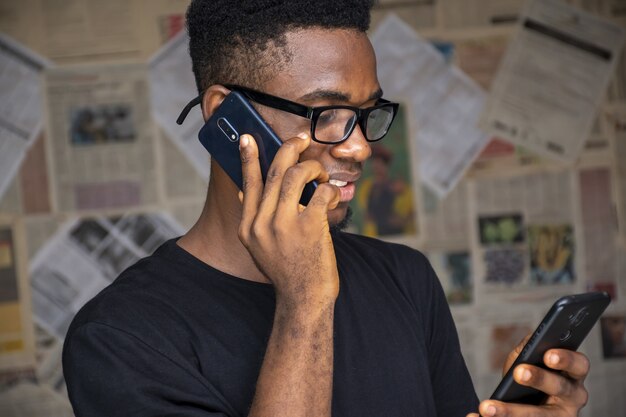 Hombre joven con gafas hablando por teléfono mientras usa otro en una habitación
