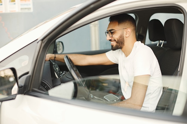 Hombre joven con gafas puliendo el interior de su coche con una alfombra. Hombre vestido con camiseta blanca