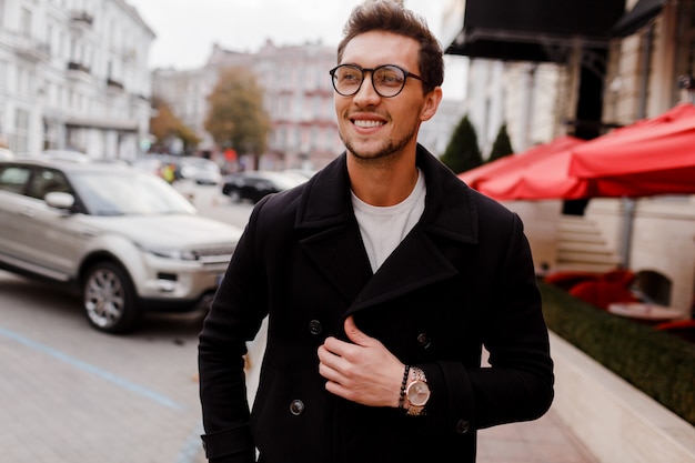 Hombre joven con gafas con ropa de otoño caminando por la calle. Chico elegante con peinado moderno en la calle urbana.