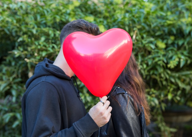 Hombre joven con globo en forma de corazón besando a mujer
