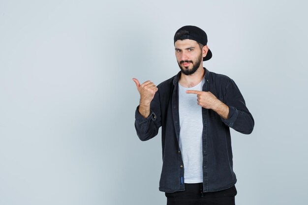 Hombre joven con gorra apuntando con el dedo y mostrando los pulgares para arriba