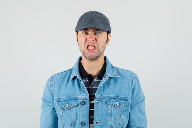 Hombre joven con gorra, camiseta, chaqueta apretando los dientes y mirando enojado