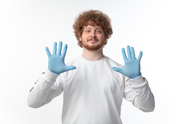 Hombre joven con guantes azules en la pared blanca