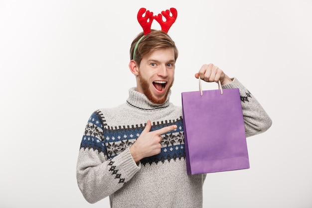 Hombre joven guapo con barba feliz con bolsa de compras en la mano aislada en blanco.