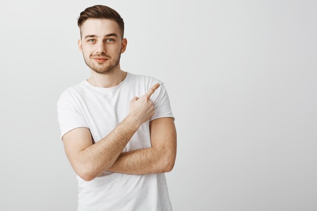 Hombre joven guapo complacido en camiseta blanca que señala el dedo en la esquina superior derecha