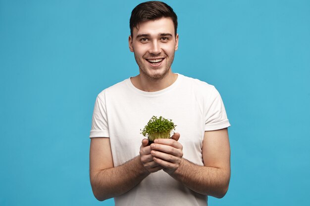 Hombre joven guapo enérgico con cerdas sosteniendo micro verdes en ambas manos