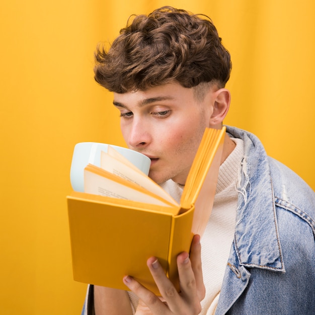 Hombre joven y guapo leyendo un libro en un escenario amarillo