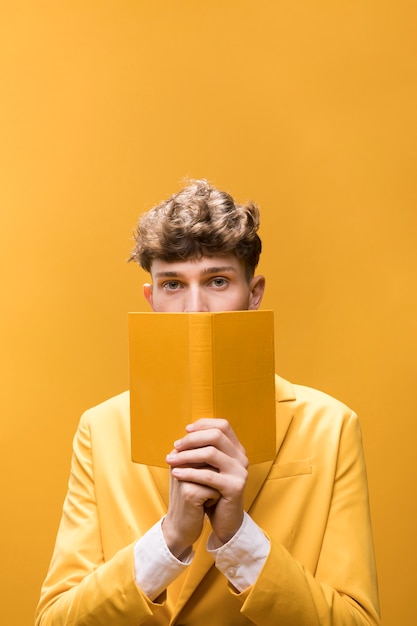 Hombre joven y guapo leyendo un libro en un escenario amarillo