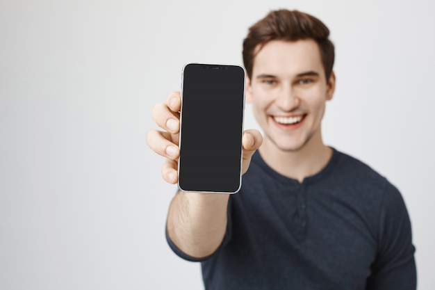 Hombre joven guapo mostrando la pantalla del teléfono móvil