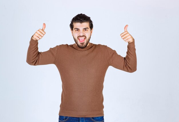 Hombre joven guapo con pulgares arriba y sonriendo.