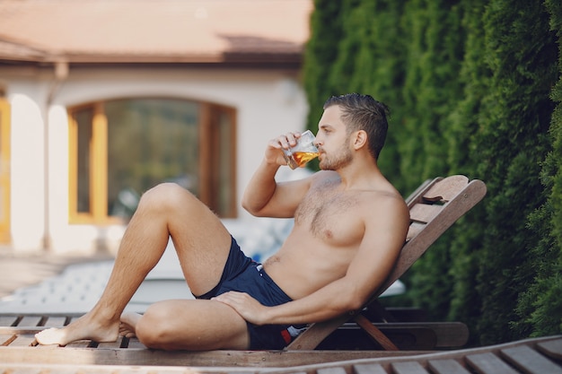 hombre joven y guapo sentado en el patio y bebiendo whisky