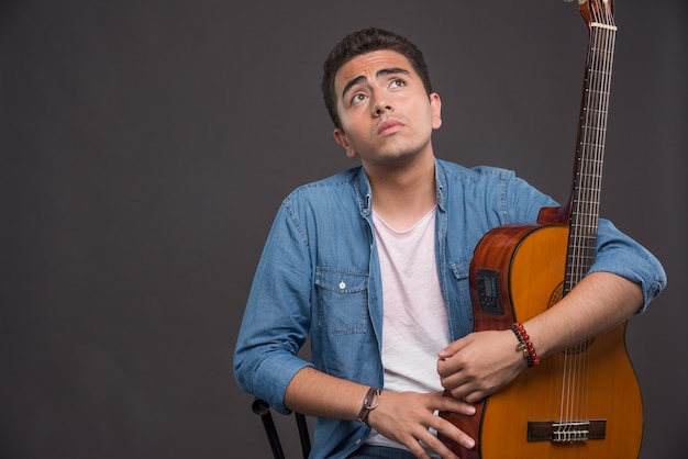 Hombre joven con guitarra mirando hacia arriba sobre fondo oscuro. Foto de alta calidad