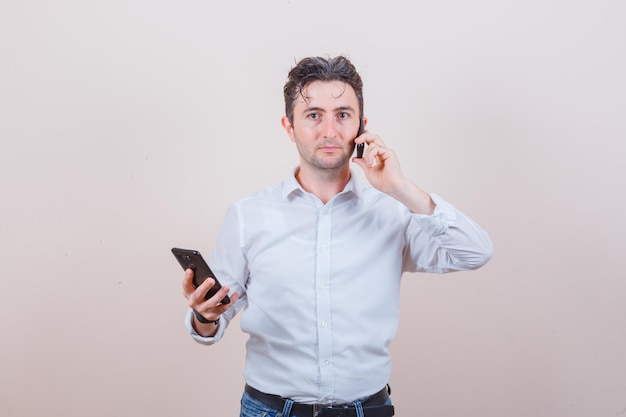 Hombre joven hablando por teléfono celular, sosteniendo el teléfono inteligente en camisa, jeans