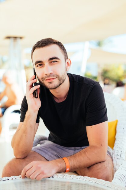 Hombre joven hablando con un teléfono inteligente en la terraza junto al mar. .