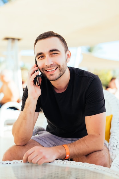 Hombre joven hablando con un teléfono inteligente en la terraza junto al mar. .