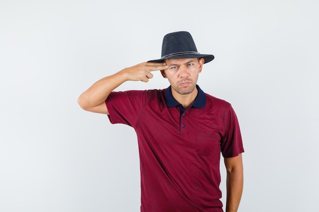 Hombre joven haciendo gesto de suicidio en camiseta, sombrero y mirando deprimido. vista frontal.