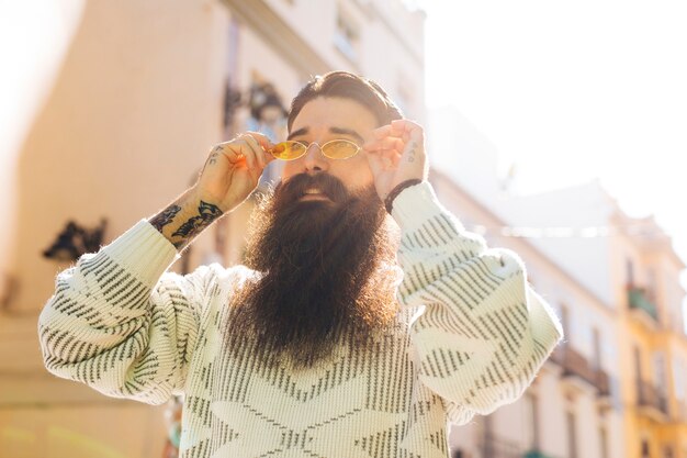 Hombre joven hermoso barbudo que pone en las gafas de sol amarillas durante verano