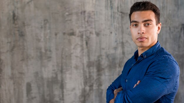 Hombre joven hermoso en la camisa azul que se opone a la pared gris