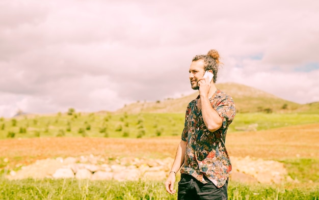 Hombre joven hermoso que habla en smartphone en campo