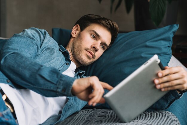 Foto gratuita hombre joven hermoso que miente en cama usando la tableta digital