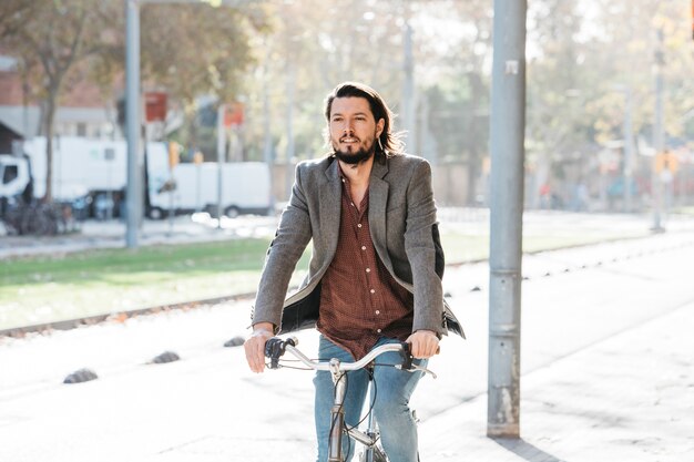 Hombre joven hermoso que monta su bicicleta en el parque