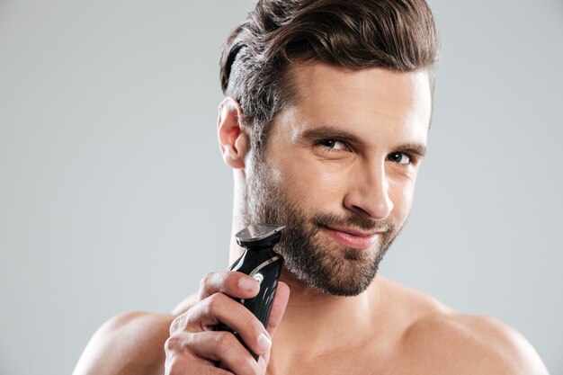 Hombre joven hermoso que sostiene la maquinilla de afeitar eléctrica