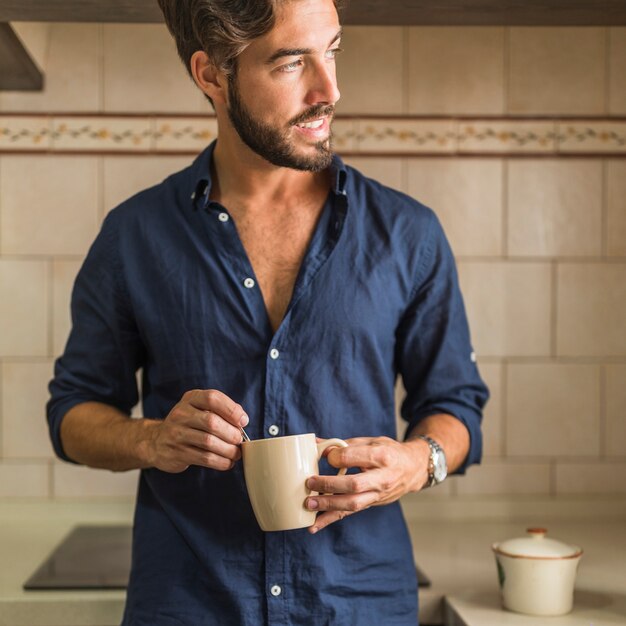 Hombre joven hermoso que sostiene la taza de café en su mano