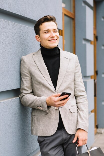 Hombre joven hermoso que sostiene el teléfono celular en la mano que mira lejos