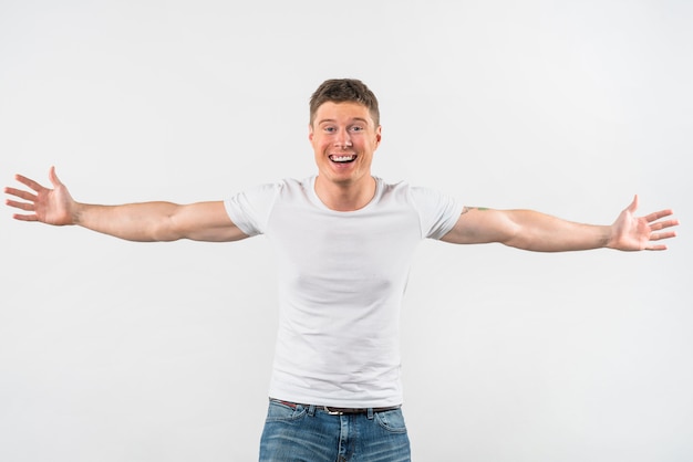 Hombre joven hermoso sonriente outstretching sus brazos aislados en el fondo blanco