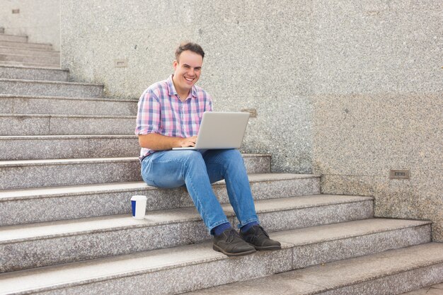 Hombre joven hermoso sonriente que mecanografía en el ordenador portátil