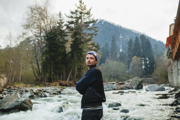 Hombre joven inconformista caminando sobre una roca en el río en el bosque de invierno