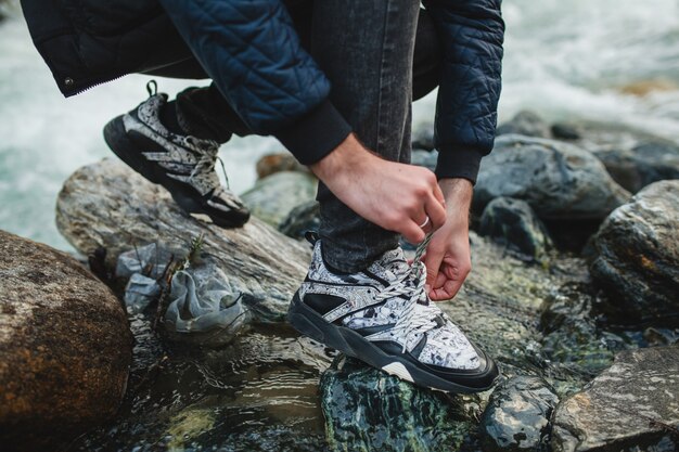 Hombre joven inconformista caminando sobre una roca en el río en el bosque de invierno