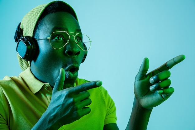 hombre joven inconformista escuchando música con auriculares en estudio azul con luces de neón. Expresión emocional
