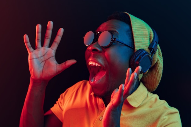 hombre joven inconformista escuchando música con auriculares en estudio negro con luces de neón.