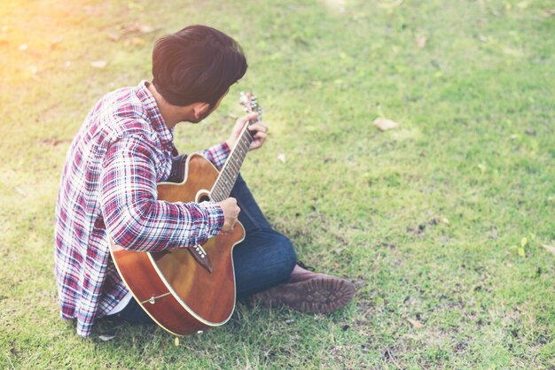 hombre joven inconformista practica la guitarra en el parque, feliz y disfrutar de p