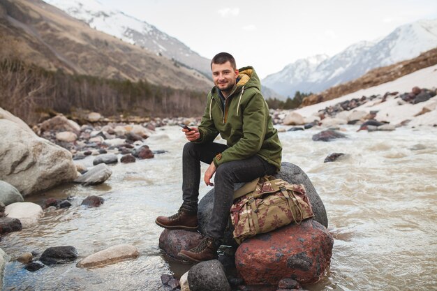 Hombre joven inconformista con smartphone, naturaleza salvaje, vacaciones de invierno, senderismo