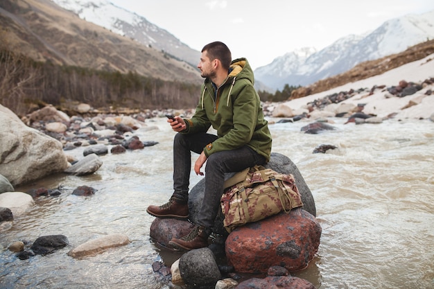 Hombre joven inconformista con smartphone, naturaleza salvaje, vacaciones de invierno, senderismo