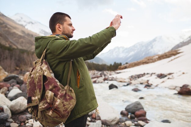 Hombre joven inconformista, tomando fotografías con smartphone, naturaleza salvaje, vacaciones de invierno, senderismo