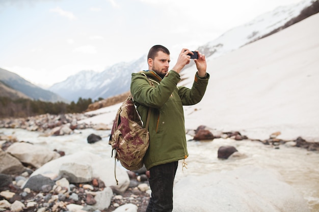 Hombre joven inconformista, tomando fotografías con smartphone, naturaleza salvaje, vacaciones de invierno, senderismo