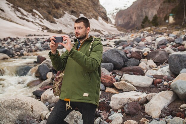 Hombre joven inconformista, tomando fotografías con smartphone, naturaleza salvaje, vacaciones de invierno, senderismo