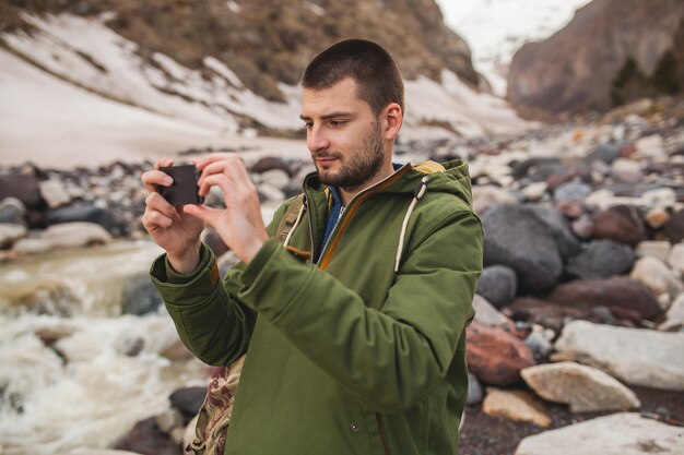 Hombre joven inconformista, tomando fotografías con smartphone, naturaleza salvaje, vacaciones de invierno, senderismo