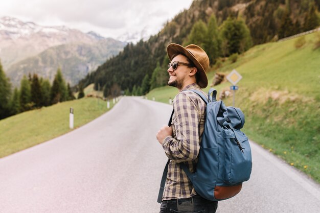 Hombre joven inspirado con una sonrisa sincera mirando a su alrededor disfrutando de la increíble naturaleza italiana y el paisaje forestal