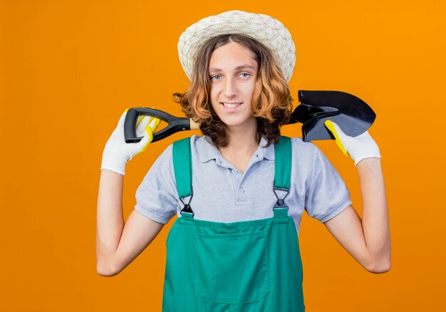 Hombre joven jardinero en guantes de goma con mono y sombrero con pala