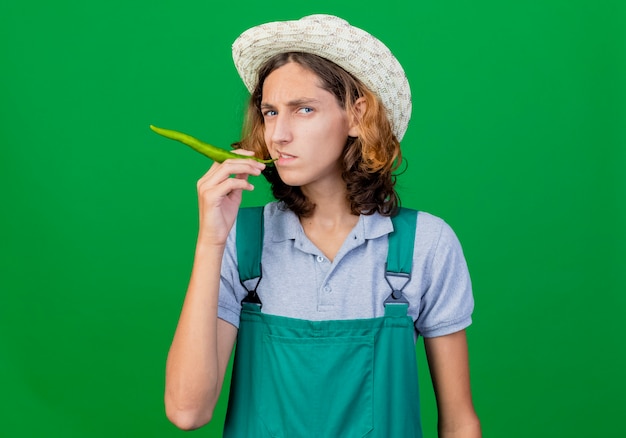 Hombre joven jardinero vestido con mono y sombrero con ají verde como cigarro