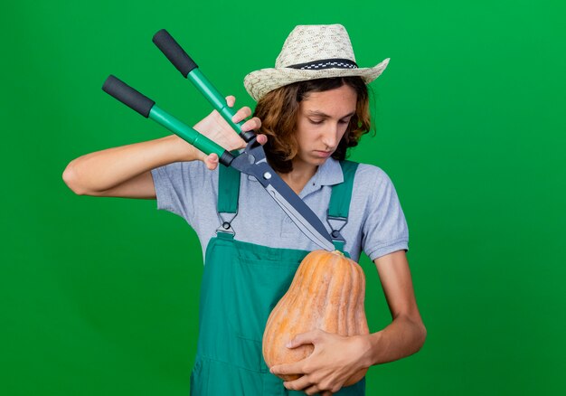 Foto gratuita hombre joven jardinero vestido con mono y sombrero con calabaza