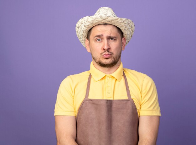 Hombre joven jardinero vestido con mono y sombrero con expresión de confianza