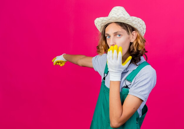 Hombre joven jardinero vestido con mono y sombrero con guantes de goma