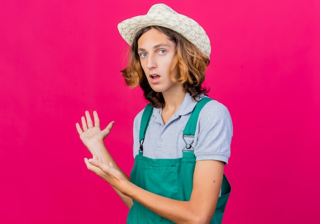 Hombre joven jardinero vestido con mono y sombrero presentando algo