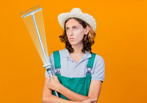 Hombre joven jardinero vestido con mono y sombrero con rastrillo