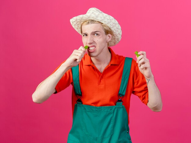 Hombre joven jardinero vestido con mono y sombrero sosteniendo mitades de ají verde